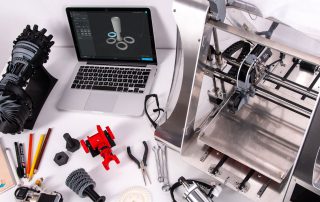 Impressora 3D ao lado de computador e outros objetos