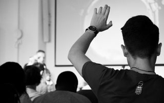 Pessoa levanta braço para fazer uma pergunta numa conferência