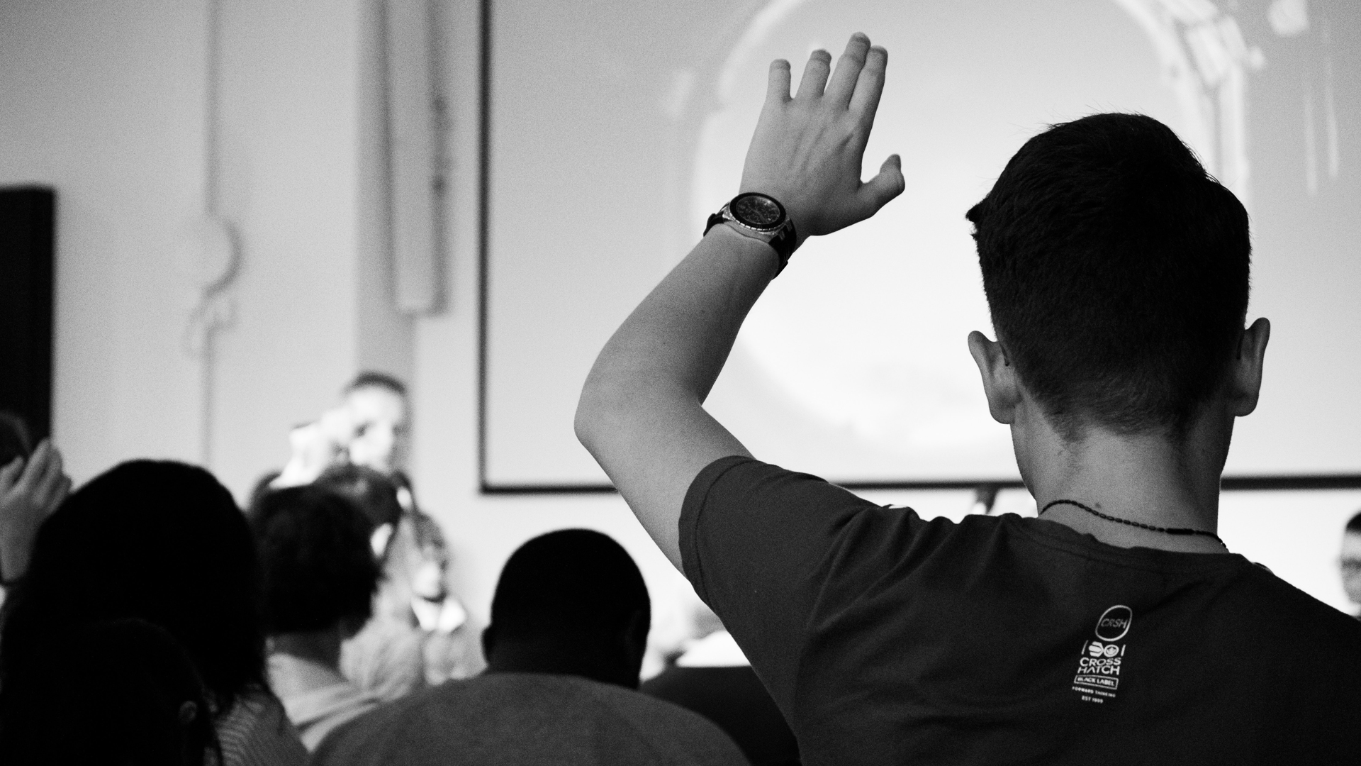 Pessoa levanta braço para fazer uma pergunta numa conferência