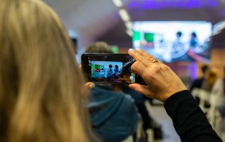 senhora a tirar foto com telemóvel em evento na casa do impacto
