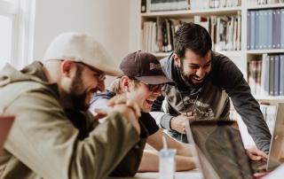 três jovens sorriem a olhar para ecrã de computador