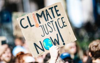 mão empunha cartaz com as palavras "climate justice now!"