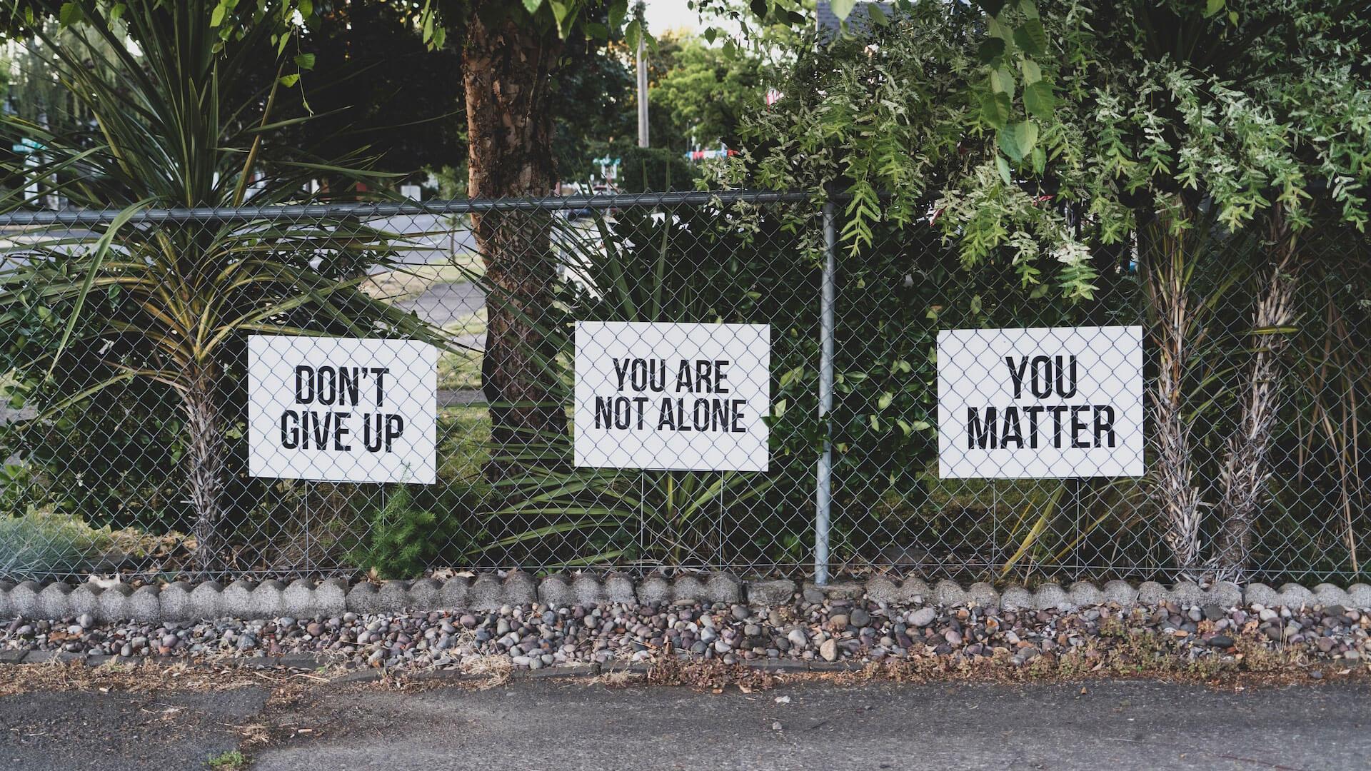 cartaz presos a cerca com as frases: "Don't Give Up"; "You are not alone"; "You matter".